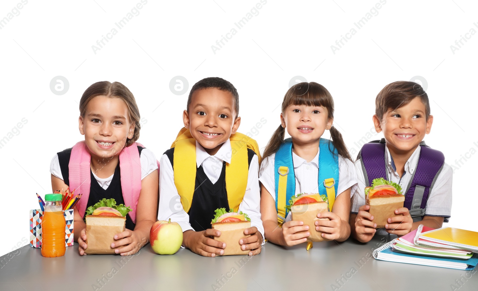 Photo of Schoolchildren with healthy food and backpacks sitting at table on white background