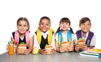 Schoolchildren with healthy food and backpacks sitting at table on white background