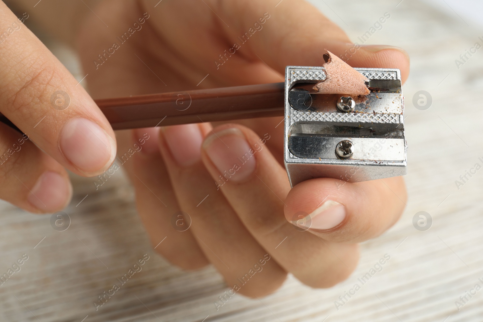 Photo of Woman sharpening pencil at wooden table, closeup
