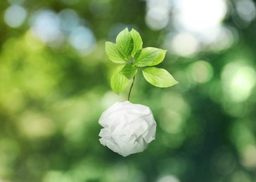 Crumpled sheet of paper on twig with green leaves on blurred background, bokeh effect. Recycling concept