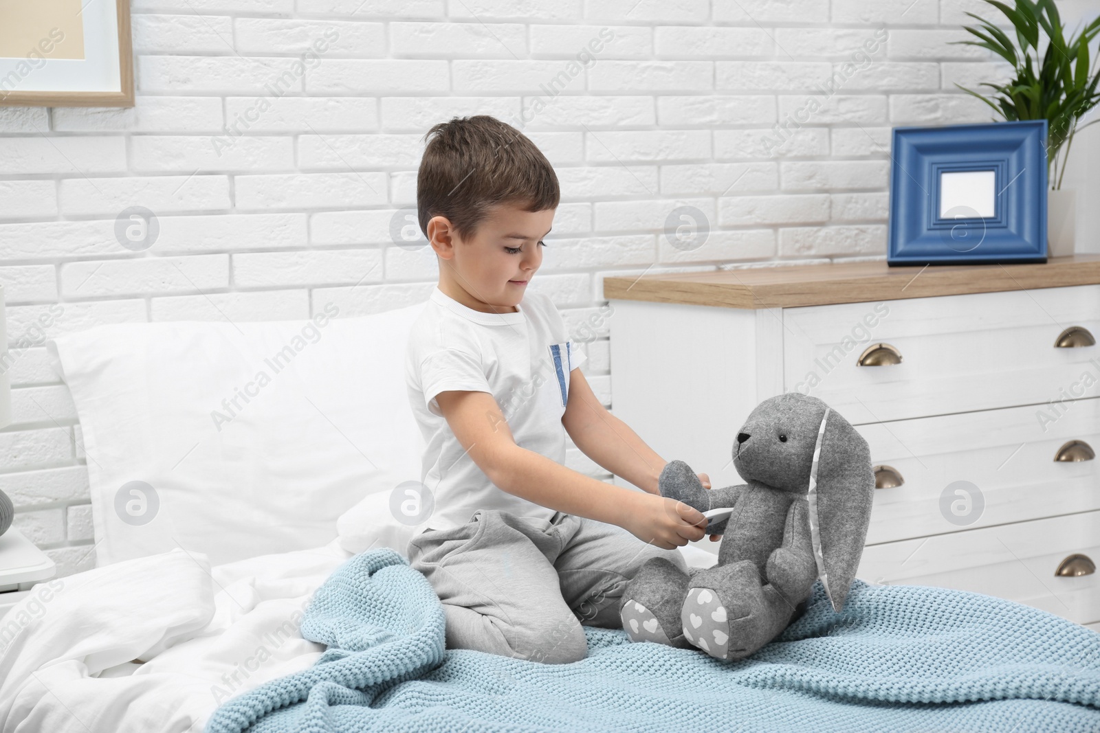 Photo of Cute child playing doctor with stuffed toy on bed in hospital ward