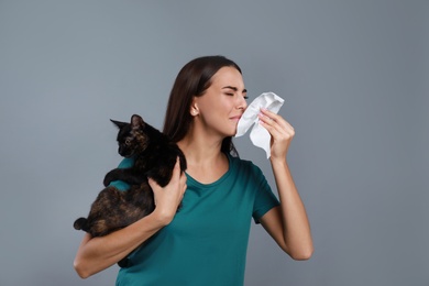 Young woman with cat suffering from allergy on grey background