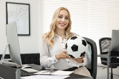 Happy woman with soccer ball at table in office