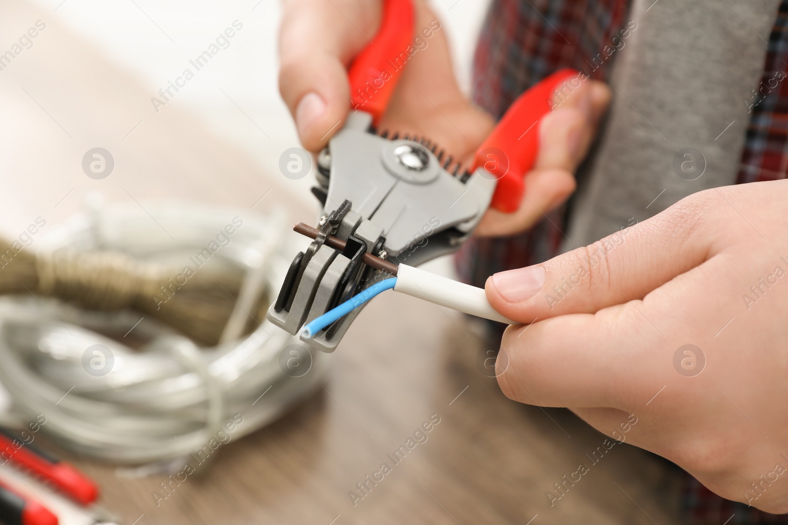 Photo of Professional electrician stripping wiring at wooden table, closeup