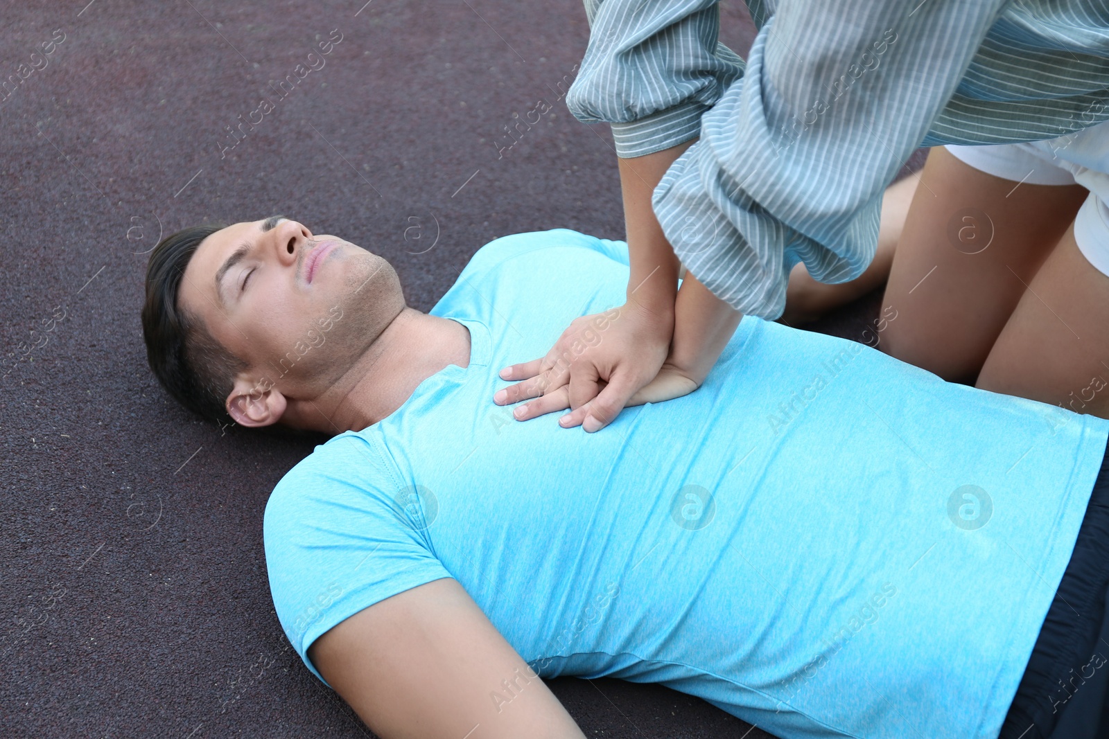 Photo of Young woman performing CPR on unconscious man outdoors. First aid