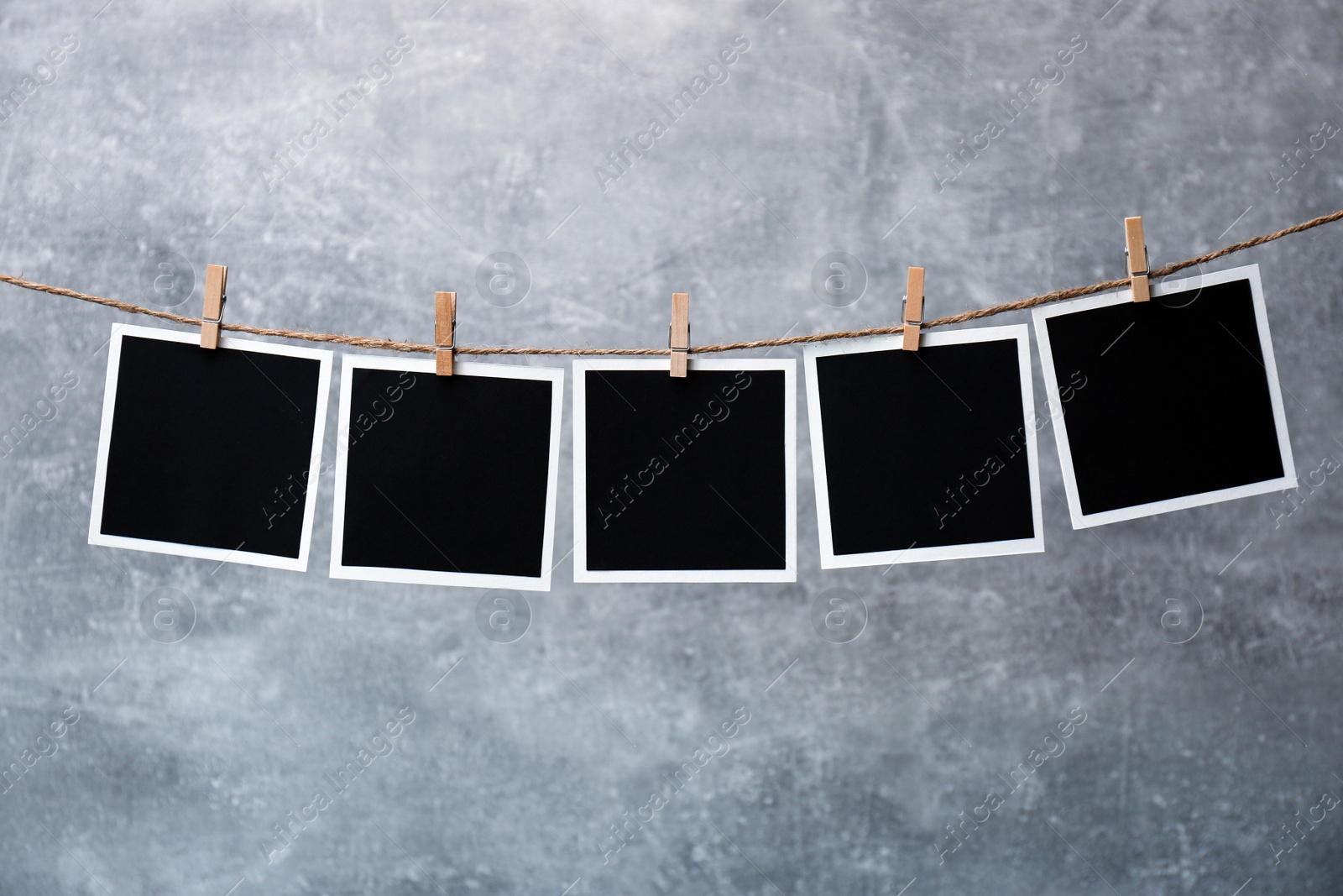 Photo of Wooden clothespins with empty instant frames on twine against grey background. Space for text