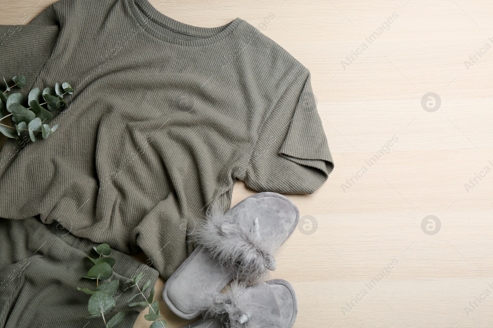 Photo of Pair of fluffy slippers, pajamas and space for text branches on wooden background, flat lay. Comfortable home outfit