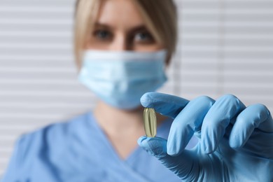 Photo of Doctor holding pill on light background, selective focus. Space for text