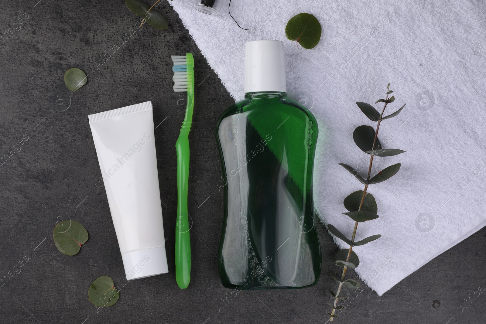 Photo of Fresh mouthwash in bottle, toothbrush and toothpaste on dark textured table, flat lay