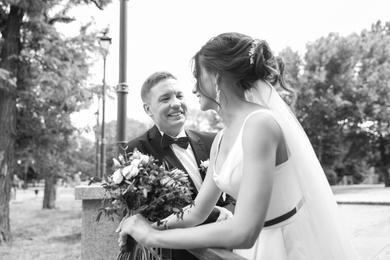 Happy newlyweds with beautiful bridal bouquet outdoors, black and white effect