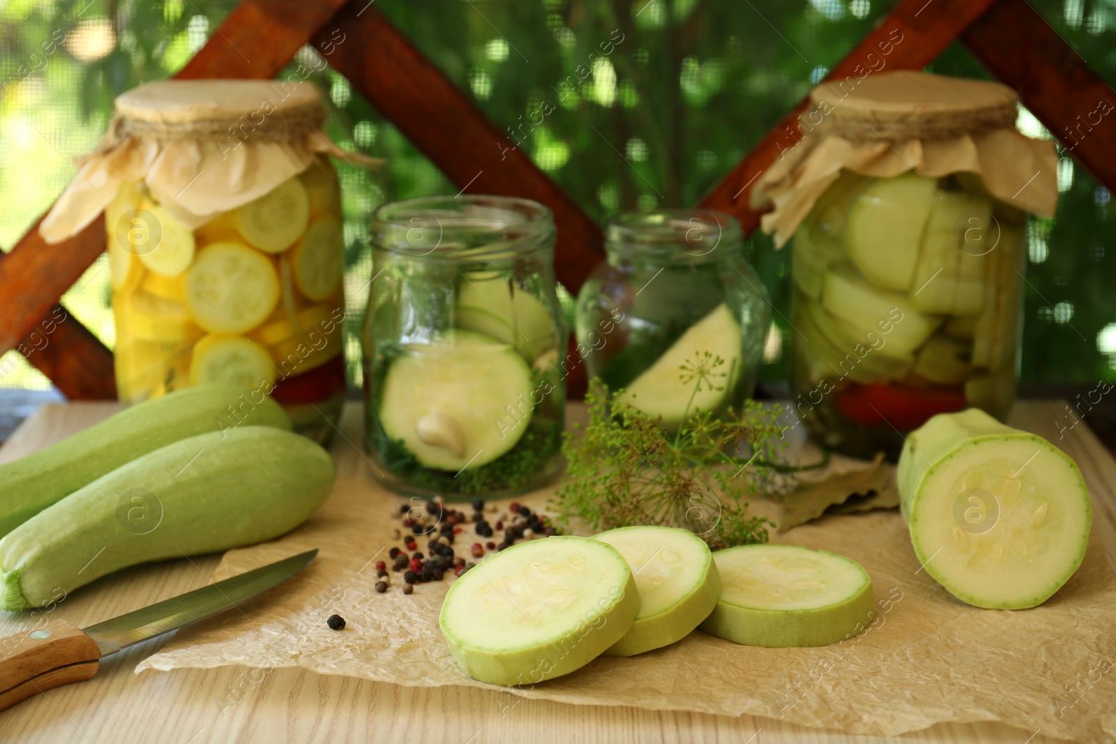 Photo of Cut fresh zucchini and jars of pickled vegetables on white wooden table