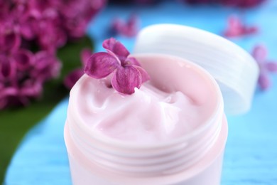 Jar of cream and lilac flowers on light blue wooden table, closeup