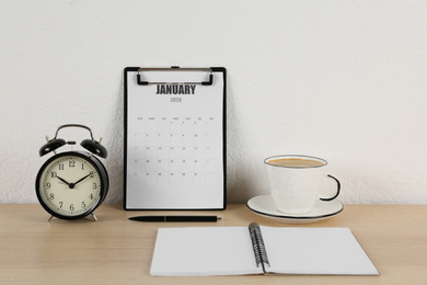 Photo of Calendar, alarm clock and cup of coffee on wooden table