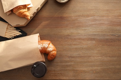 Photo of Paper bags with pastry and takeaway food on wooden table, top view. Space for text