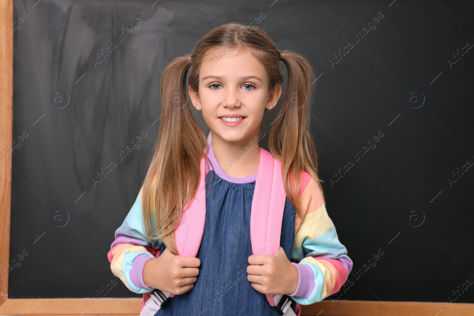 Photo of Back to school. Smiling girl with backpack near blackboard