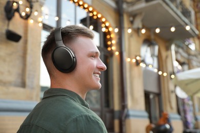 Photo of Smiling man in headphones listening to music outdoors. Space for text