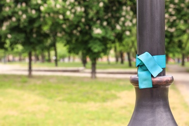 Teal awareness ribbon tied on lamppost in park, space for text