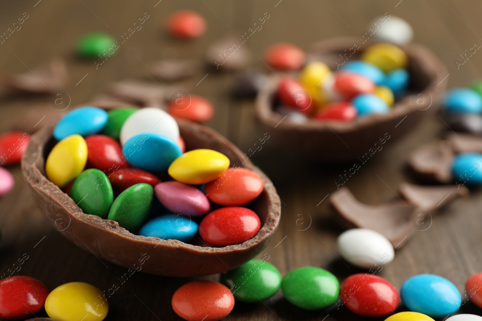 Photo of Broken chocolate egg and colorful candies on wooden table, closeup