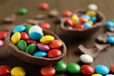 Photo of Broken chocolate egg and colorful candies on wooden table, closeup