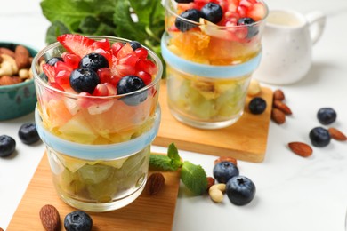 Photo of Delicious fruit salad, fresh berries, mint and nuts on white marble table