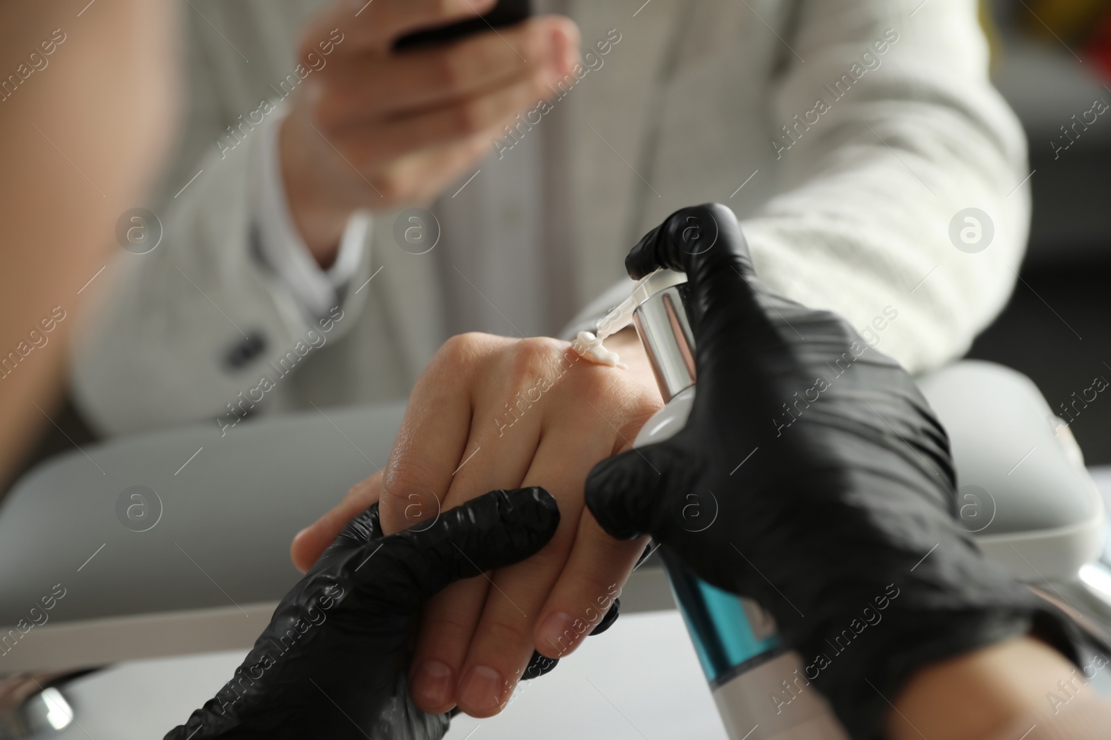 Photo of Professional manicurist applying cream on client's hand in beauty salon, closeup