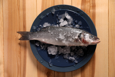 Photo of Fresh raw fish with ice on wooden table, top view