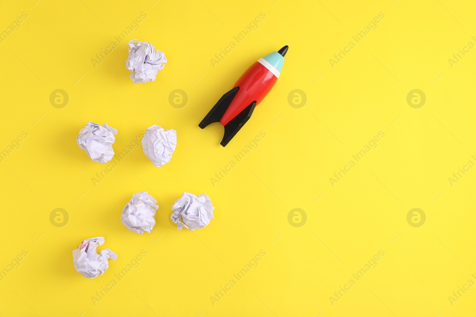 Photo of Toy rocket and crumpled paper on yellow background, flat lay with space for text. Startup concept