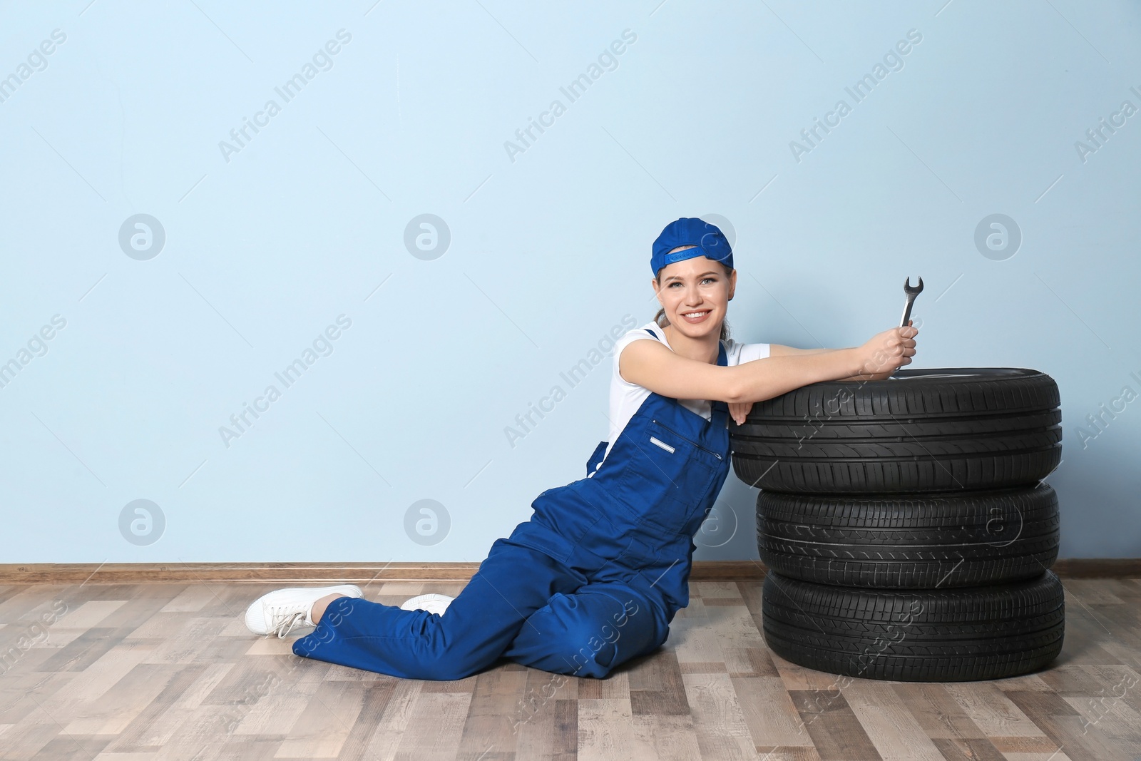 Photo of Female mechanic with car tires on grey wall background