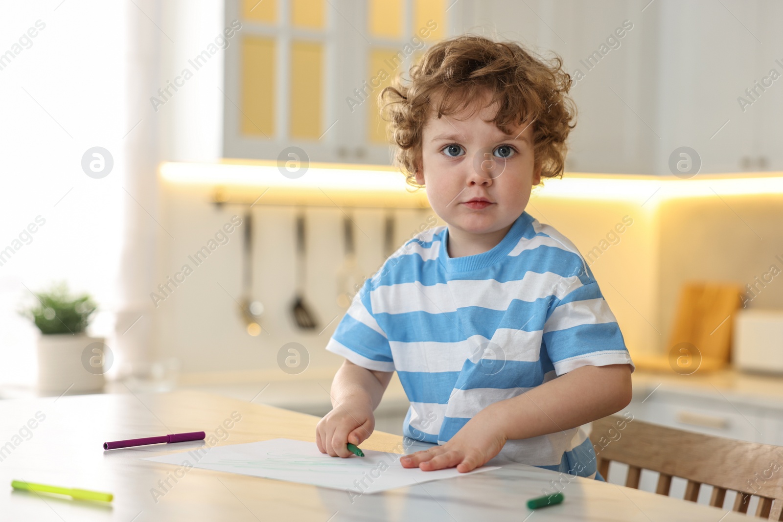 Photo of Cute little boy drawing with marker at table in kitchen. Space for text