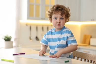 Cute little boy drawing with marker at table in kitchen. Space for text