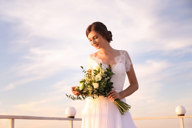 Gorgeous bride in beautiful wedding dress with bouquet near river