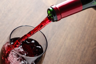 Pouring tasty red wine in glass at wooden table, closeup