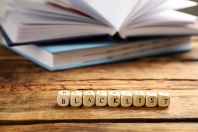 Cubes with word Blacklist and notebooks on wooden table, closeup