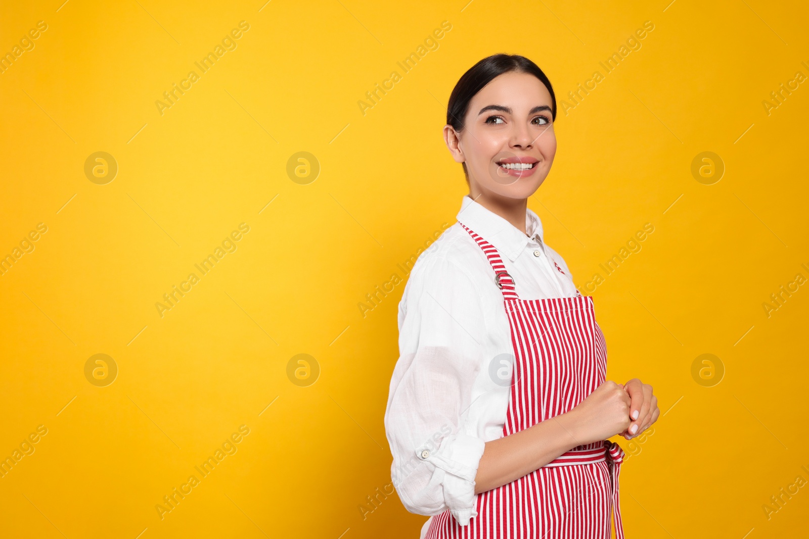 Photo of Young woman in red striped apron on yellow background, space for text