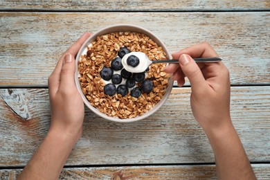 Woman eating yogurt with granola and blueberries on old wooden table, top view