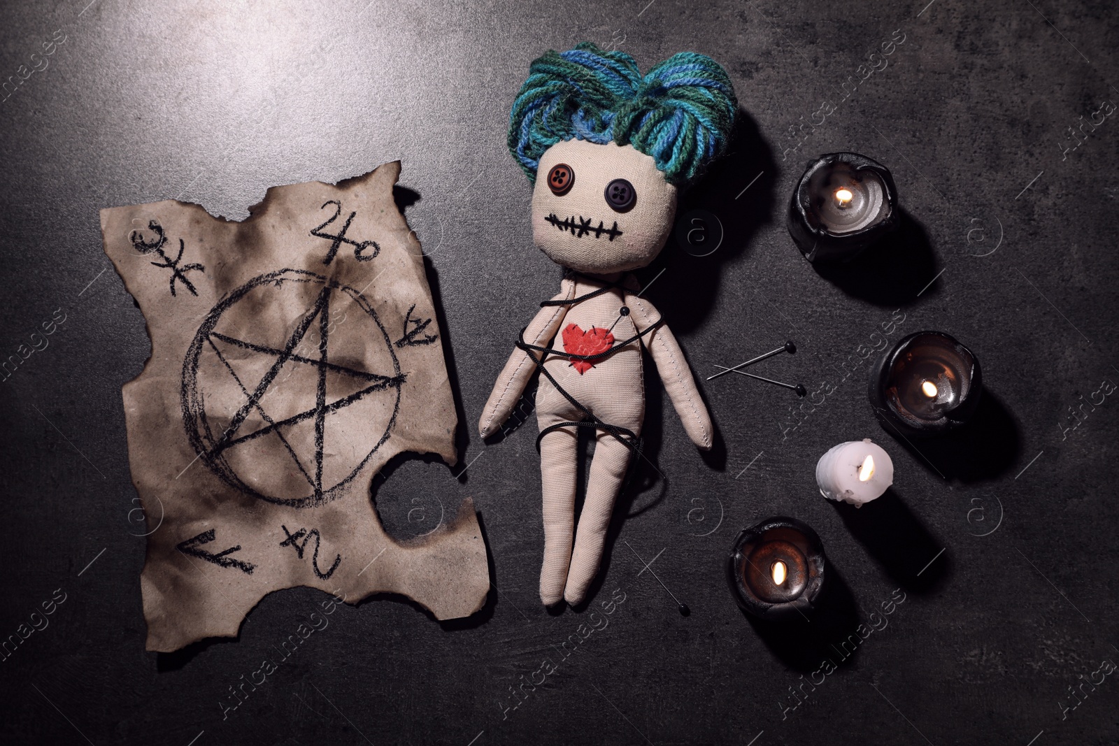 Photo of Female voodoo doll with pin in heart and ceremonial items on grey table, flat lay