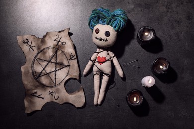 Photo of Female voodoo doll with pin in heart and ceremonial items on grey table, flat lay