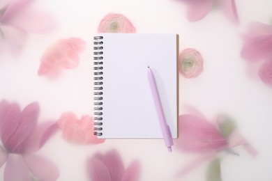 Guest list. Notebook and pen on spring floral background, top view