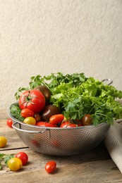 Wet vegetables in colander on wooden table, closeup. Space for text