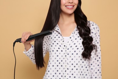 Photo of Happy woman using hair iron on beige background, closeup
