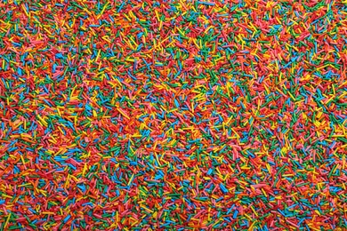 Photo of Bright colorful sprinkles as background, top view. Confectionery decor