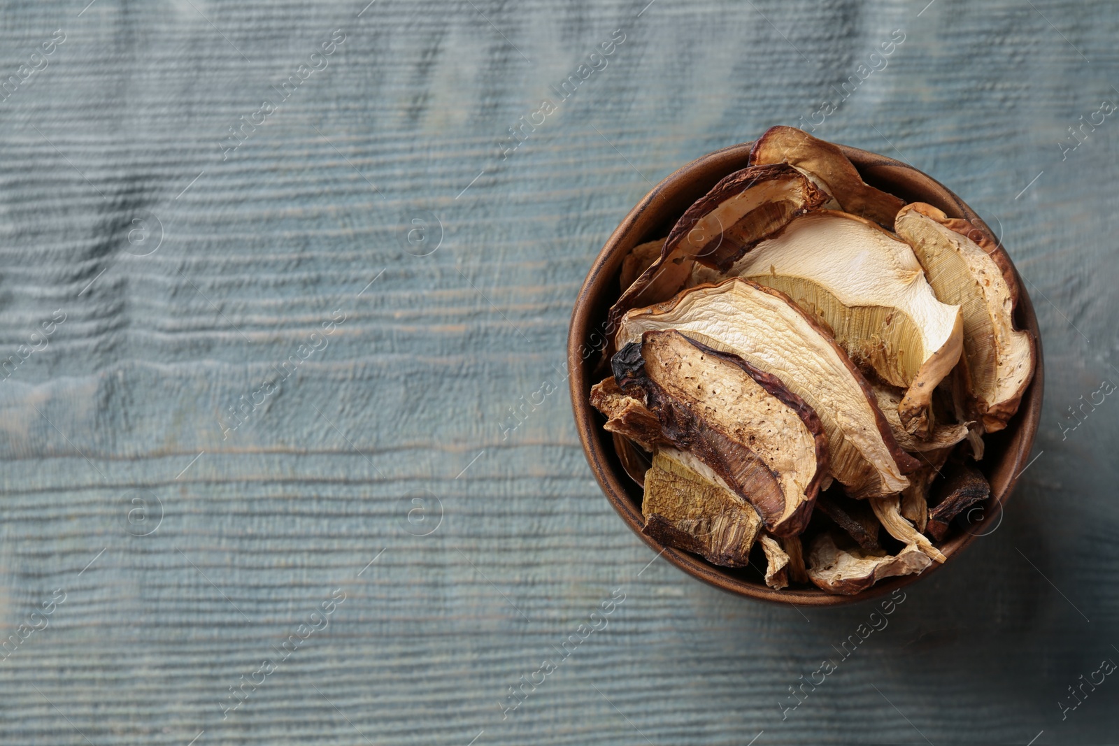 Photo of Bowl of dried mushrooms on color wooden background, top view with space for text