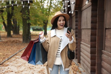 Special Promotion. Emotional young woman with shopping bags and smartphone on city street