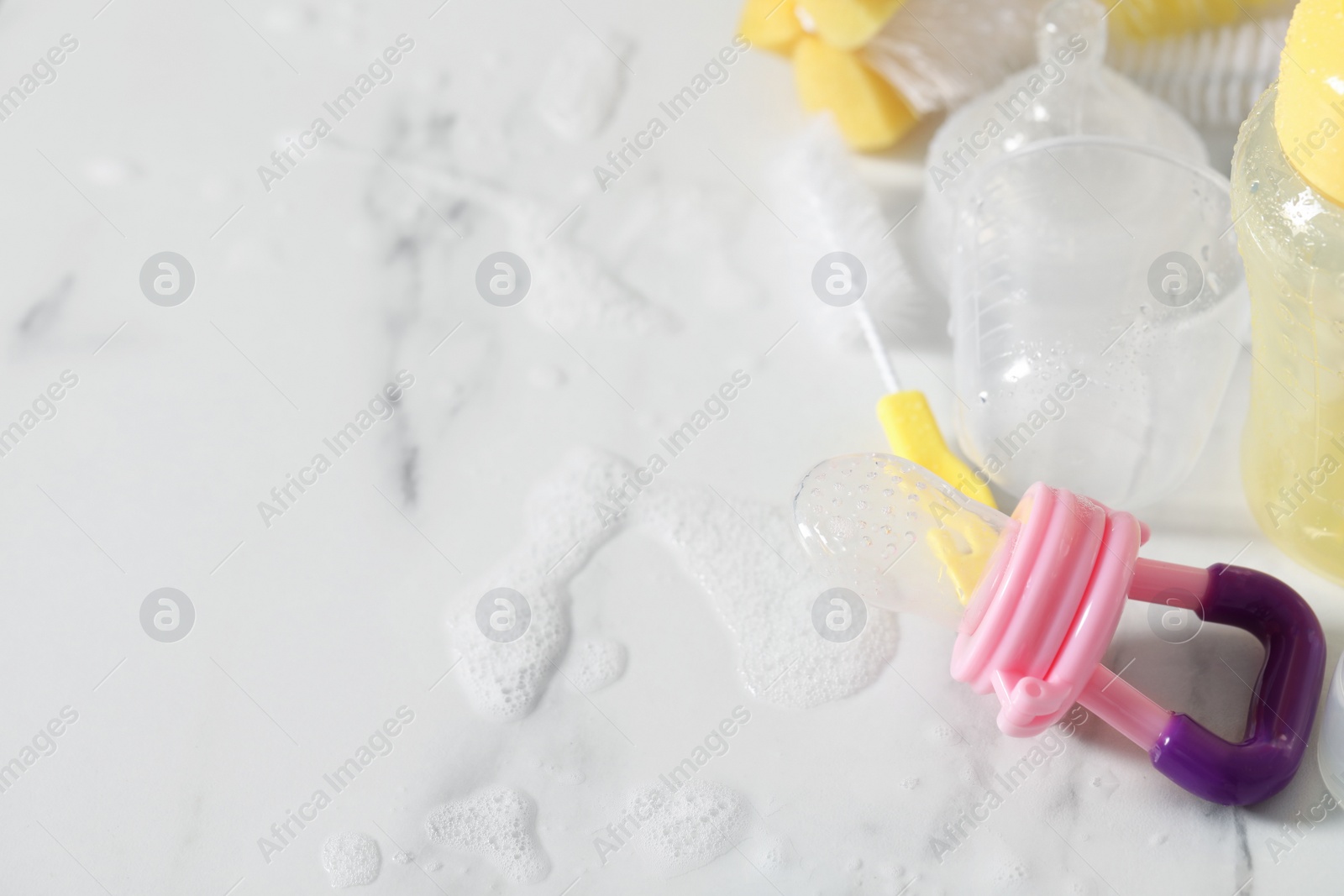 Photo of Clean pacifier after sterilization near brush on wet white table, above view. Space for text