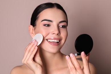 Photo of Beautiful young woman applying face powder with puff applicator on dusty rose background