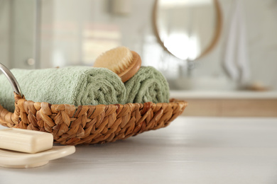 Photo of Wicker basket with rolled towels on white wooden table in bathroom. Space for text