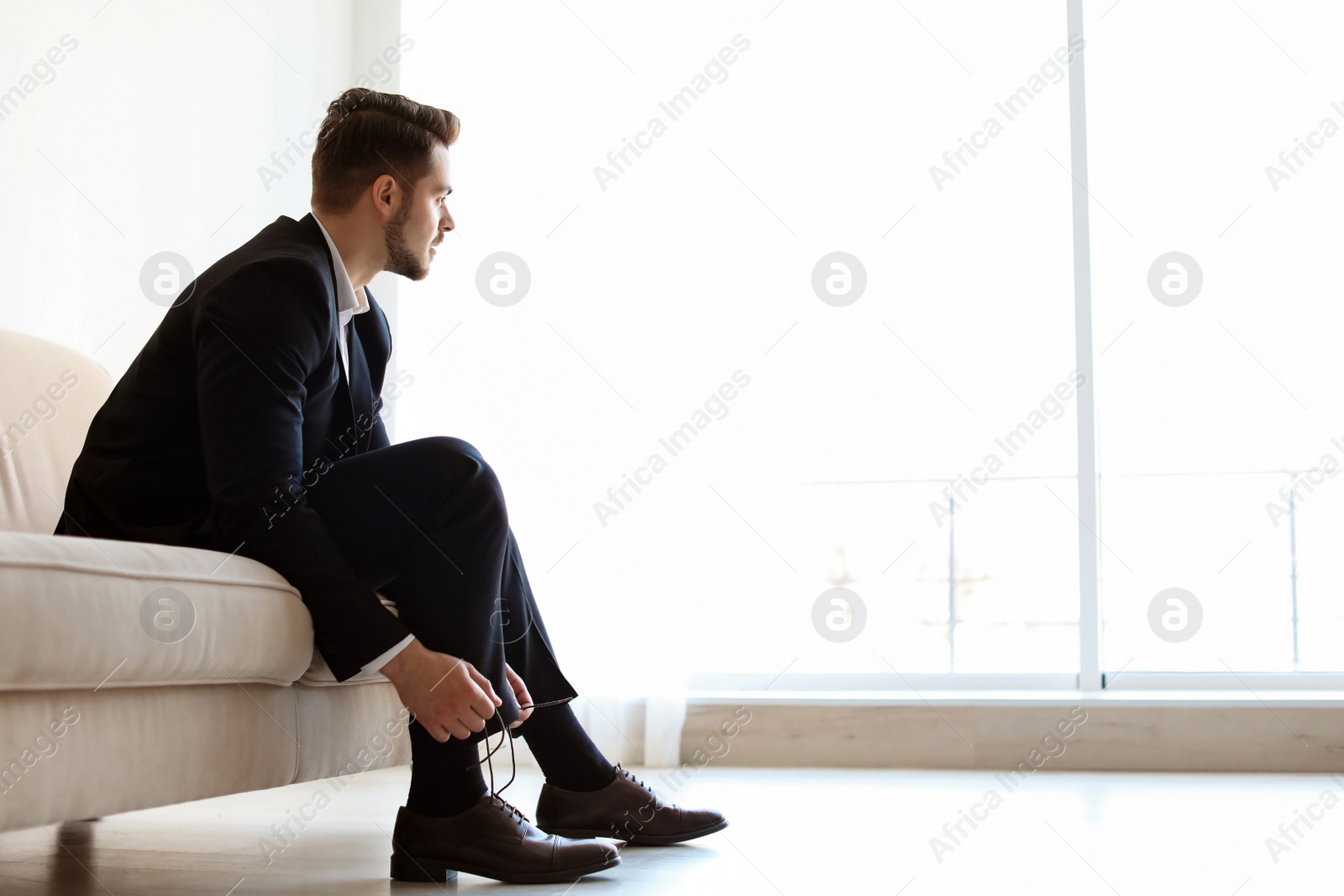 Photo of Young man putting on elegant leather shoes indoors