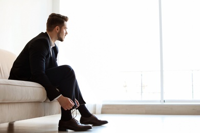 Photo of Young man putting on elegant leather shoes indoors