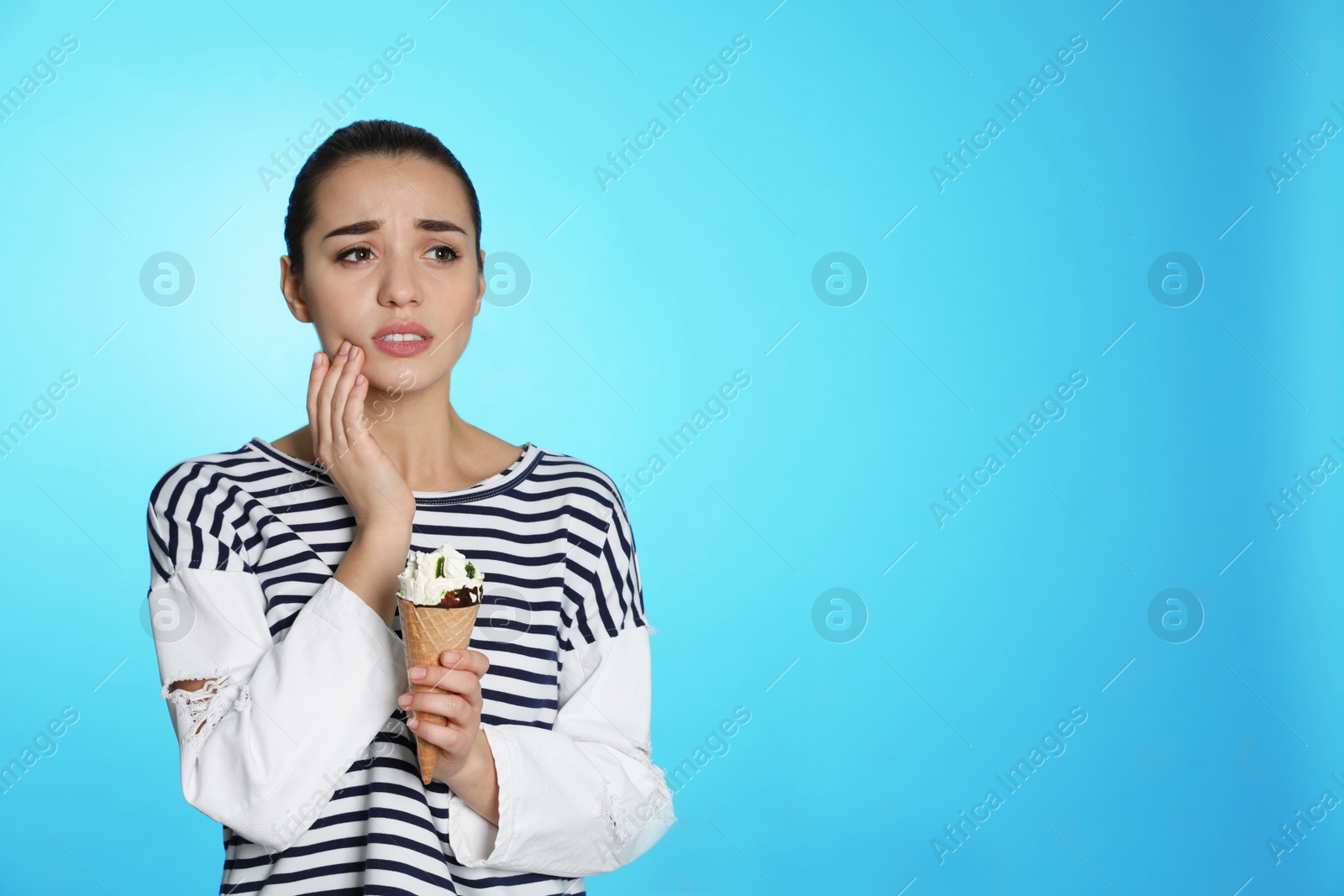 Photo of Emotional young woman with sensitive teeth and ice cream on color background. Space for text