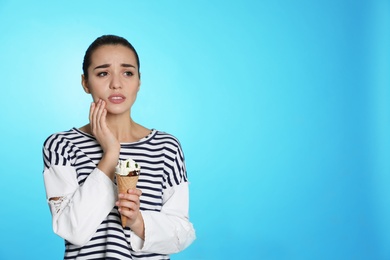 Emotional young woman with sensitive teeth and ice cream on color background. Space for text